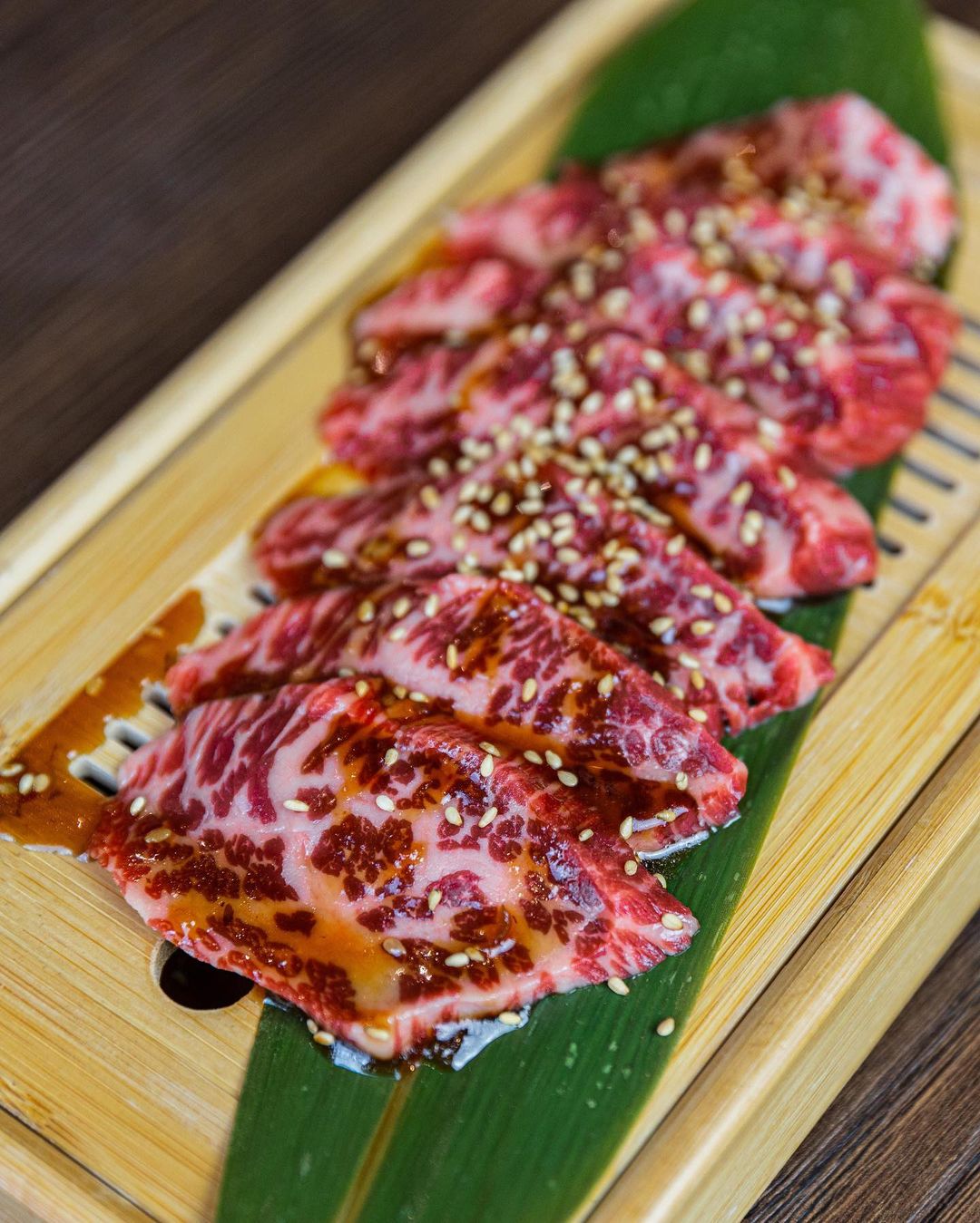 Marbled wagyu sliced thin on a bamboo leaf — sashimi-style cut for the grill
