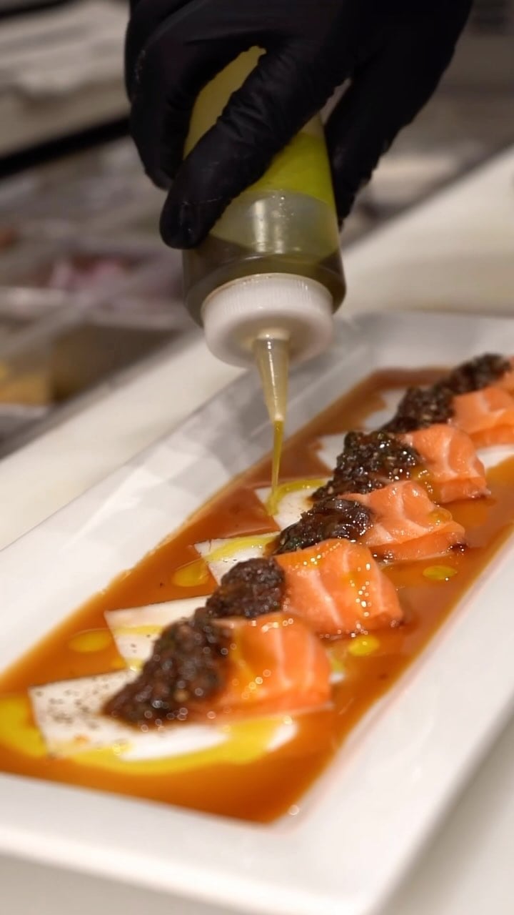 Hands finishing salmon nigiri tableside with sauce and oil