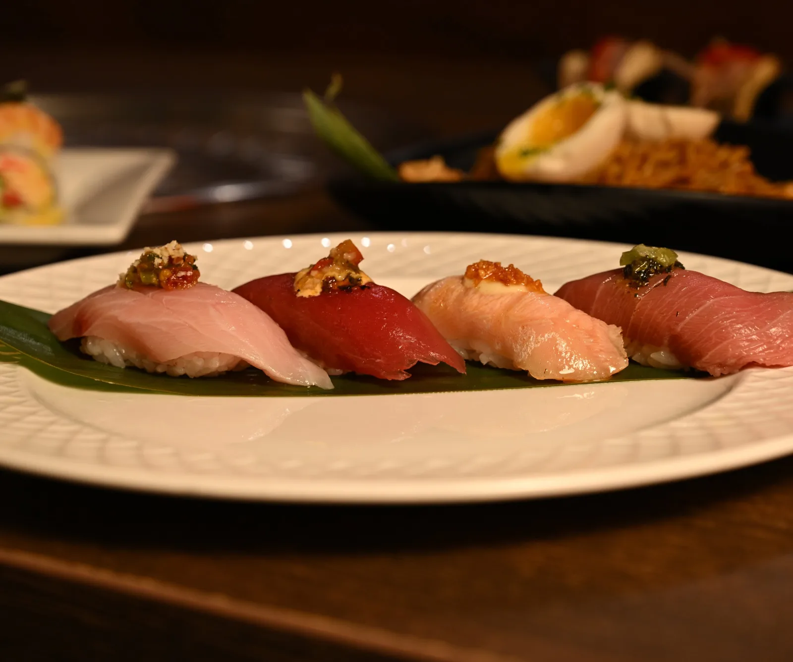 A flight of four nigiri on a white plate