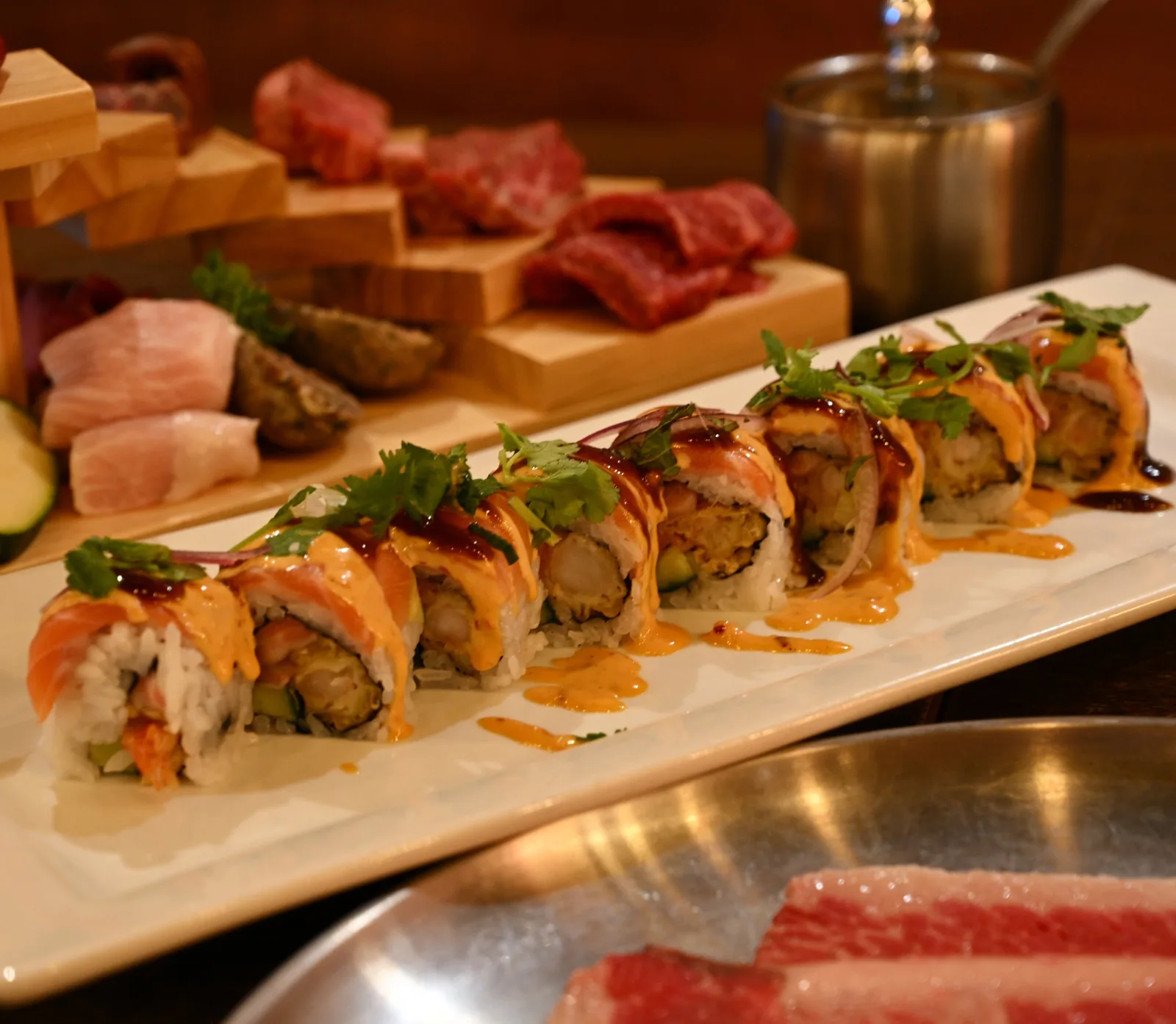 A salmon-topped roll with a spread of raw wagyu cuts behind it
